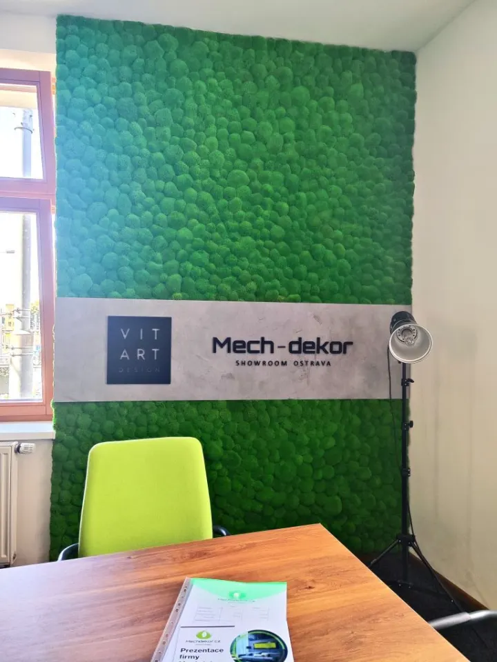 Showroom s mechovou stěnou, dřevěným pultem s logem Mech-dekor a zelenou kancelářskou židlí