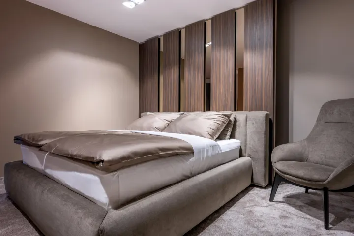 Postel Sykora Beds v ložnici s dřevěnými panely a křeslem